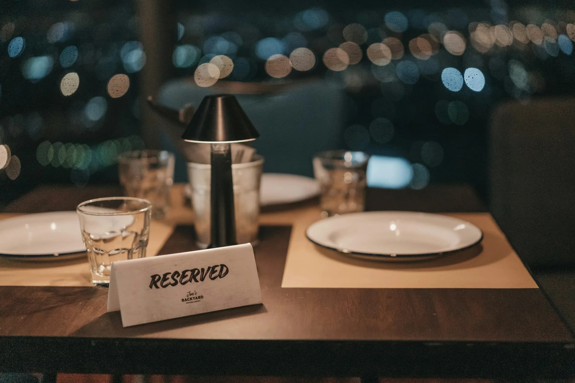 A “Reserved” card on a laid restaurant table at night, city lights out of focus behind it