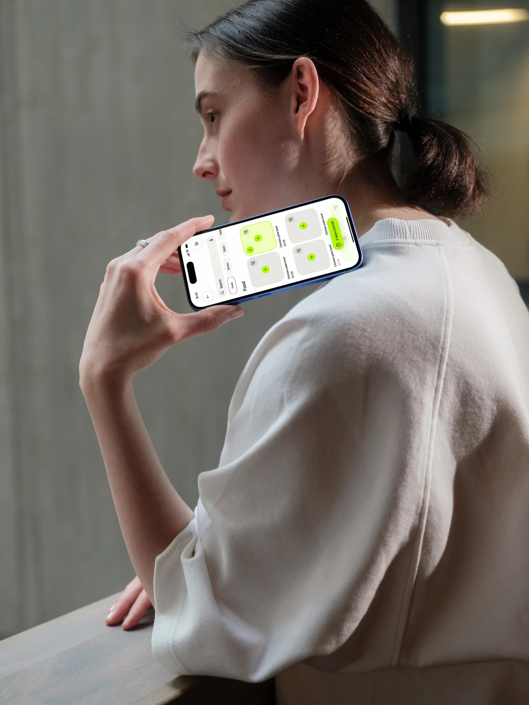 A woman in a white sweatshirt holds a phone to her shoulder, the Tapp point of sale open on its screen